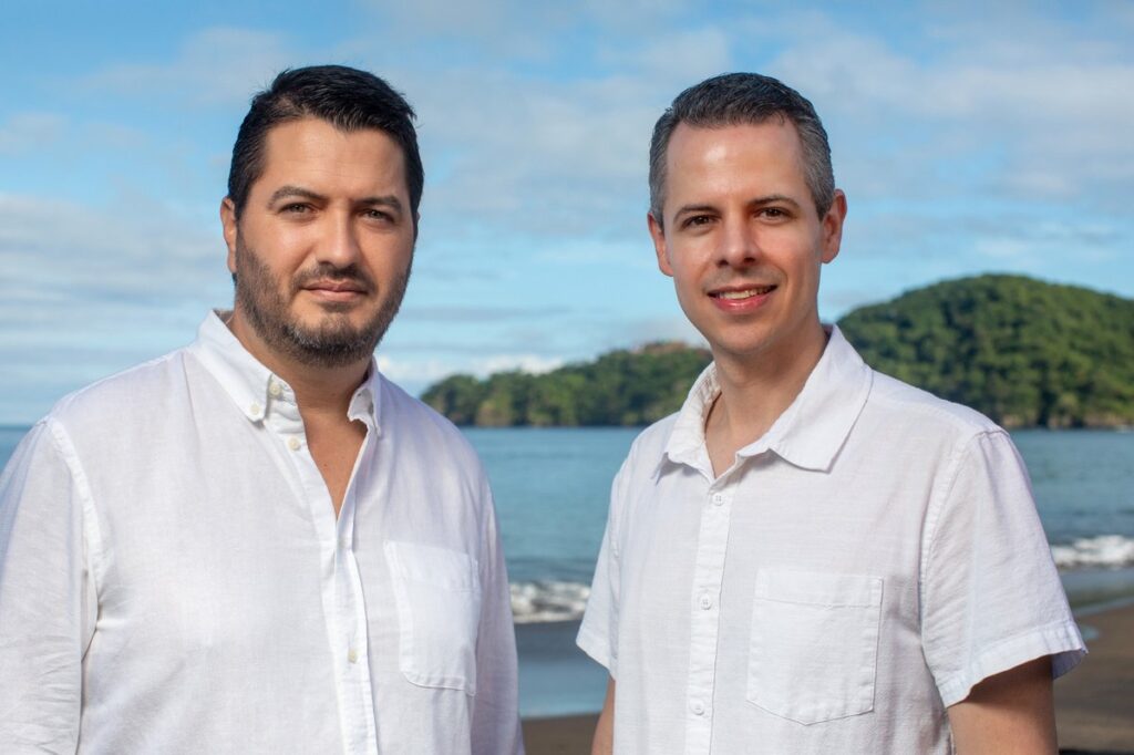 two mean, Roberto and Esteban, standing by the ocean with green mountains in the background